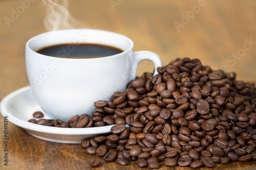 Cup of coffee,surrounded with coffee beans,on a wooden table.