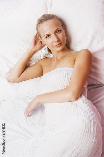 Beautiful blonde girl in white nightgown lying on the bed