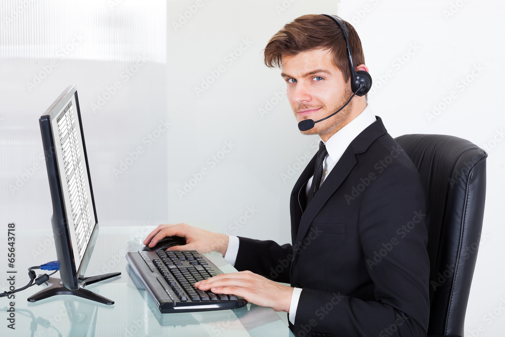 Confident Businessman In Headset Using Computer At Desk Confident Businessman In Headset Using Computer At Desk