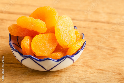 Bowl of dried apricots on wooden table background.