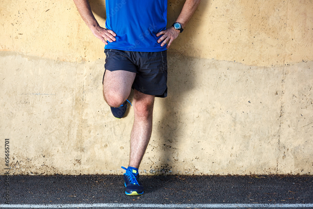 Male runner leaning relaxed against wall.