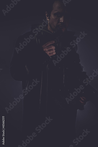dark portrait of stylish man with long leather jacket, gun armed
