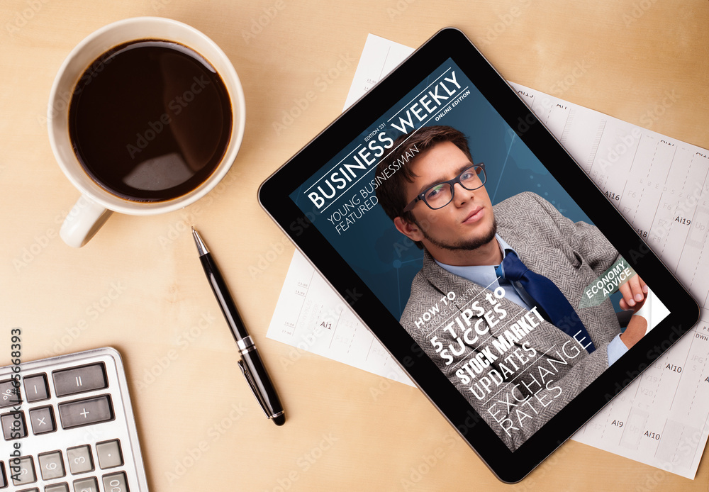 Tablet pc showing magazine on screen with a cup of coffee on a d