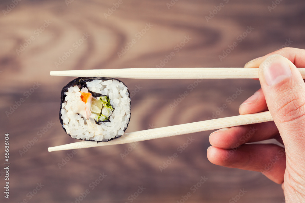 Hand holding sushi roll using chopsticks