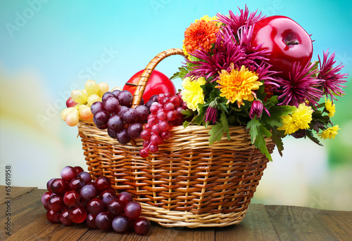 Composition with beautiful flowers in wicker basket and fruits 
