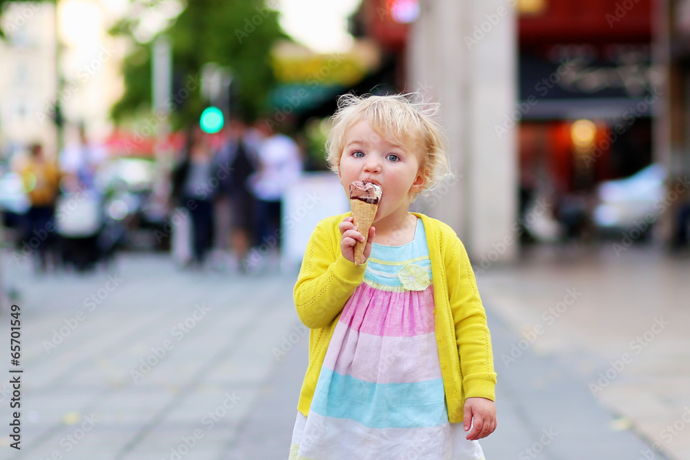 Cute little girl eating ice-cream in the center of crowed street