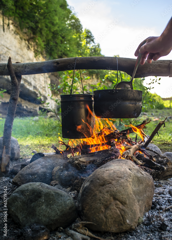 Man stirs ladle food that is prepared in a hike in the cauldrons Man stirs ladle food that is prepared in a hike in the cauldrons