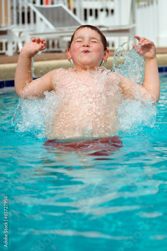 Young boy splashing into pool while swimming