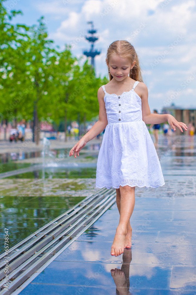 Little cute girl walking in open street fountain at hot sunny