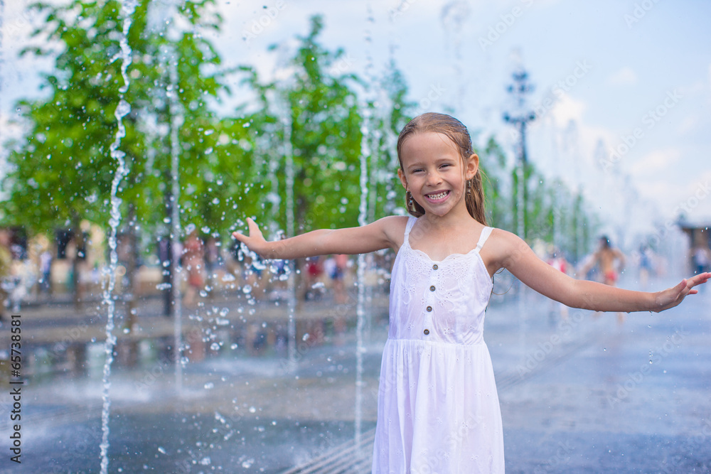 Portrait of little wet happy girl in street fountain at hot