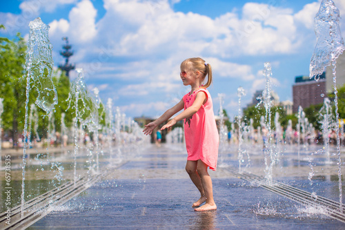 Little adorable girl have fun in street fountain at hot sunny