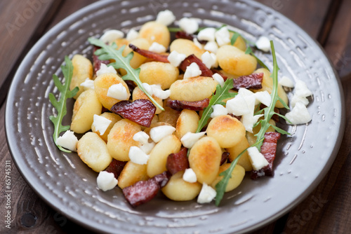 Roasted gnocchi with cheese, meat and arugula in a glass plate