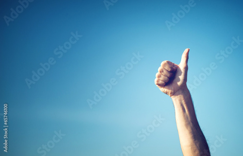 Hand showing thumbs up against blue sky
