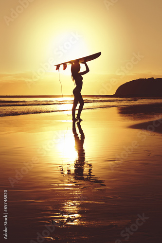 Silhouette of surfer at sunrise on beach with surfboard