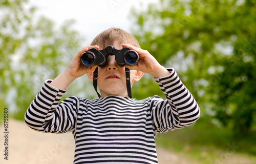 Little boy scanning the woods with binoculars