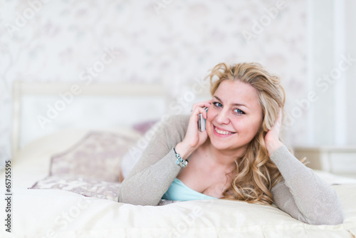 Natural cheerful blonde lying on bed and phoning in bright bedro