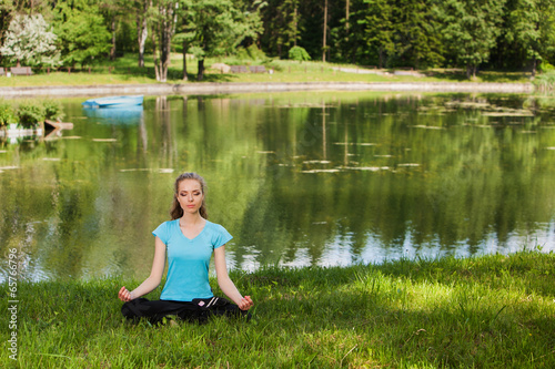 Beautiful young woman mediteting on coast of wood lake
