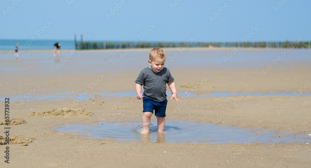 little boy splashes in a pool on the beach