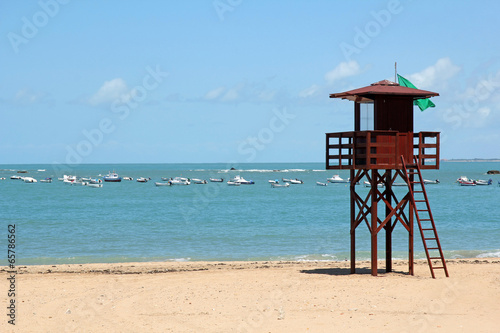 beach with lifeguard post and fishing boats in the background