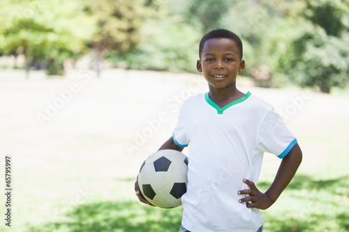 Little boy holding football in the park smiling at camera