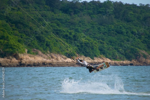 Male kite surfer jumping against wooded shore