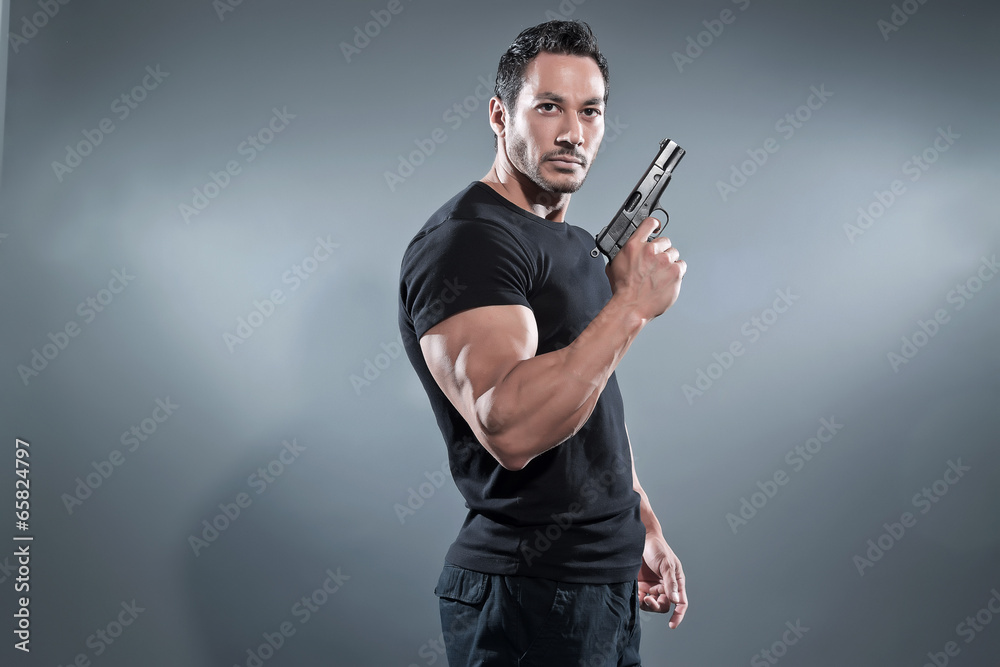 Action hero muscled man holding a gun. Wearing black t-shirt and