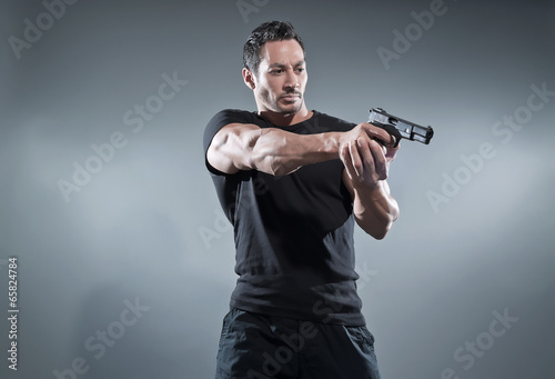 Action hero muscled man shooting with gun. Wearing black t-shirt