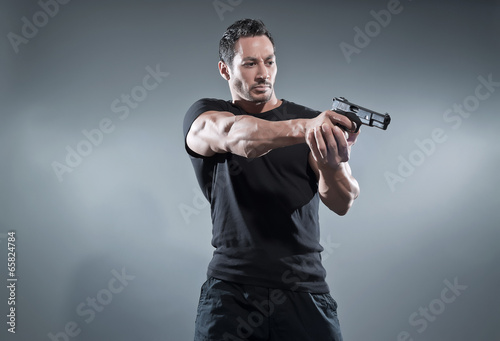 Obraz na płótnie Action hero muscled man shooting with gun. Wearing black t-shirt w salonie