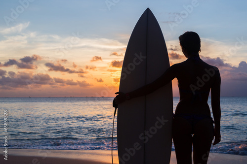 woman surfer with surfboard on tropical beach at sunset