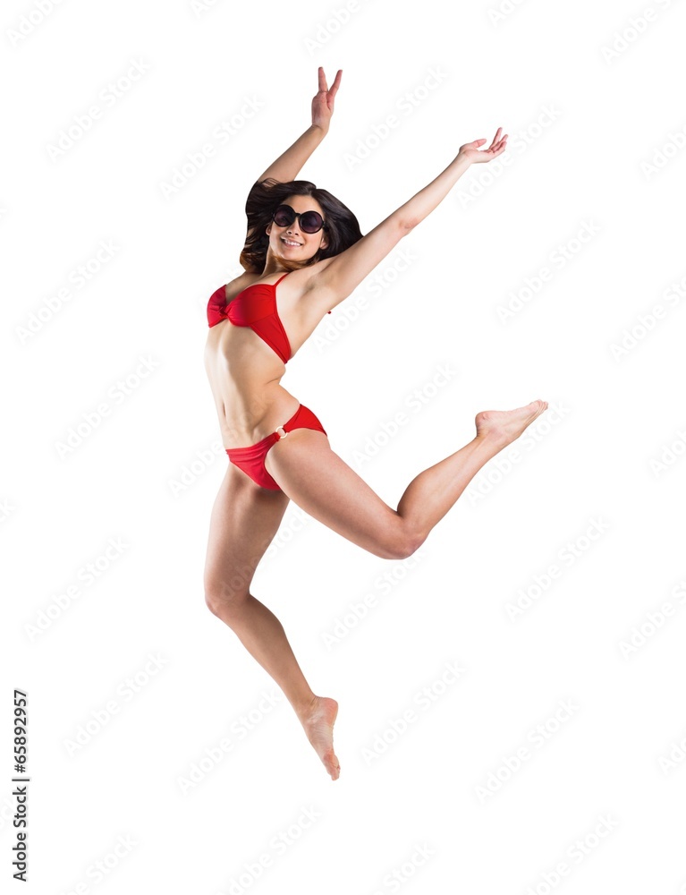 Fit girl in red bikini smiling and leaping