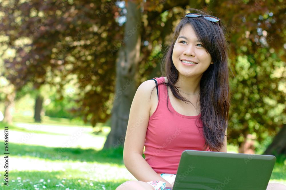 Obraz premium Smiling asian girl with a laptop at the park