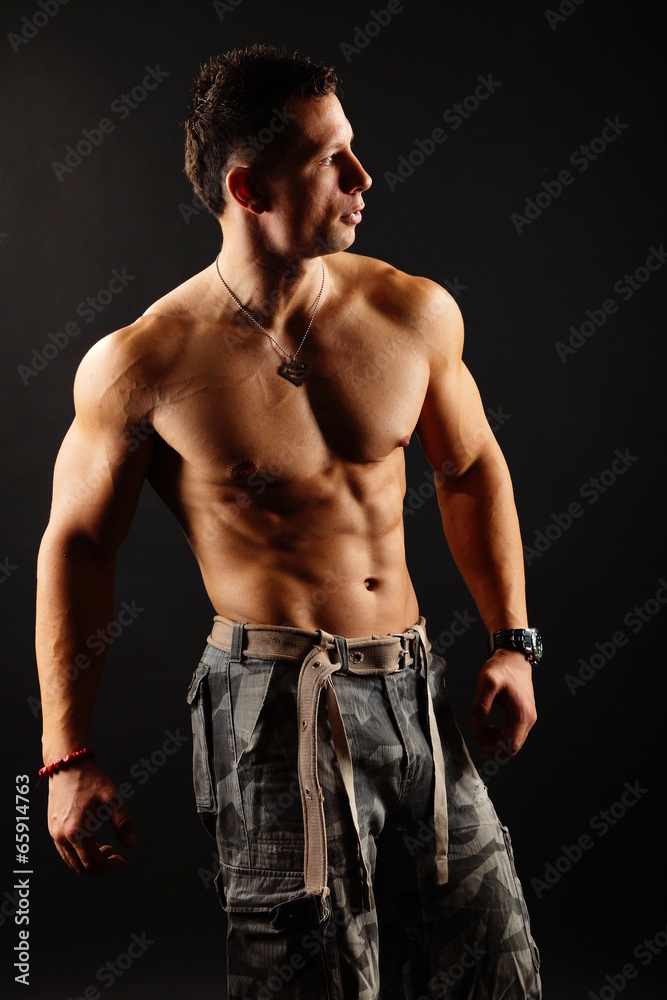 Fototapeta premium Handsome muscular man poses on the dark background
