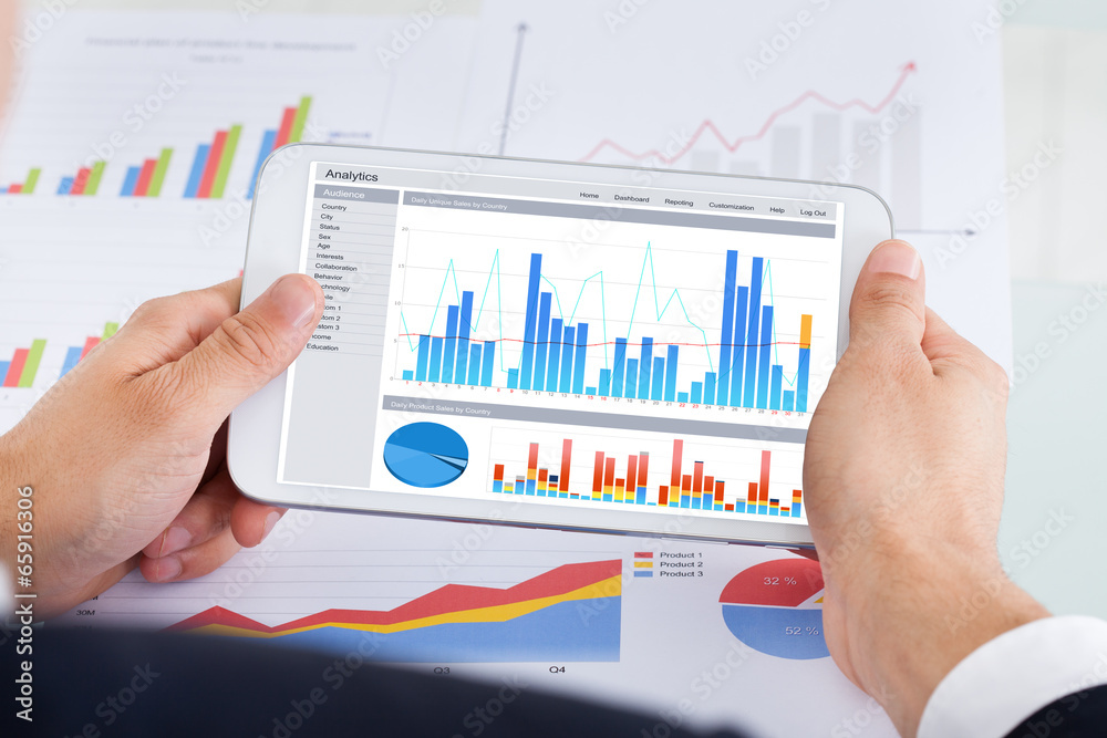 Businessman Comparing Graphs On Digital Tablet At Office Desk Businessman Comparing Graphs On Digital Tablet At Office Desk