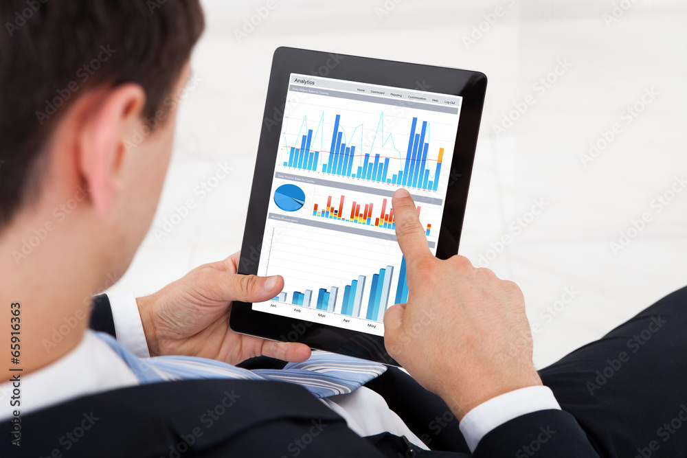Businessman Comparing Graphs On Digital Tablet In Office Businessman Comparing Graphs On Digital Tablet In Office