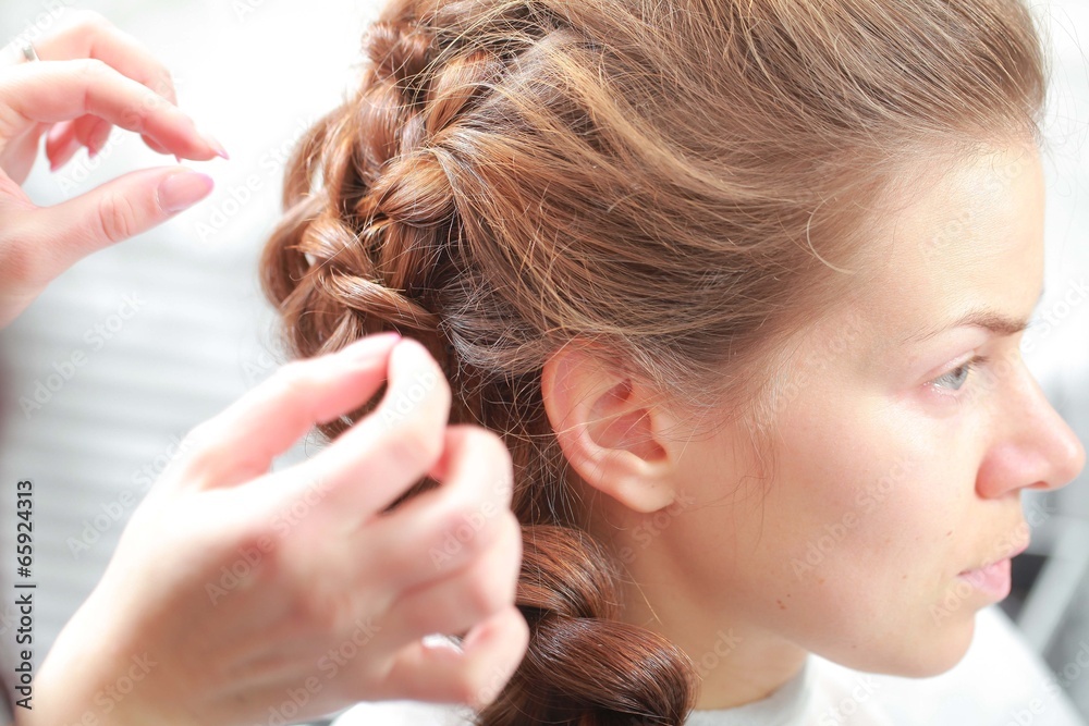 Fototapeta premium styling curls and weaving French braid on long hair in salon