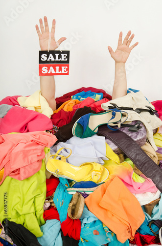 Man hands with sale sign reaching out from a big pile of clothes