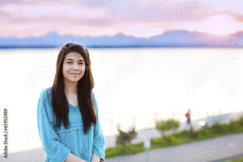Beautiful young teen girl enjoying outdoors by lake at sunset