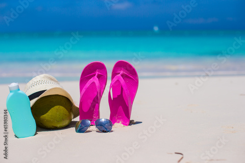 Flip flops, coconut, hat and suncream on white sand
