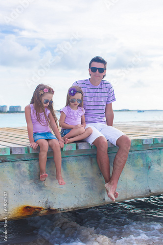 Family of three sitting on wooden dock enjoying ocean view
