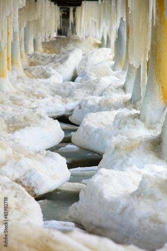Winter. Close up ice formations icicles on pier poles #65982718