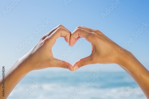 Female hands making heart shape by the sea