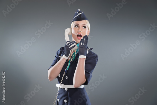 Calling retro blonde stewardess wearing blue suit. Holding white