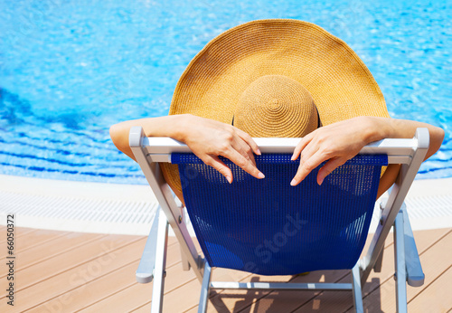 Canvas Print Young woman lying on deckchair by swimming pool