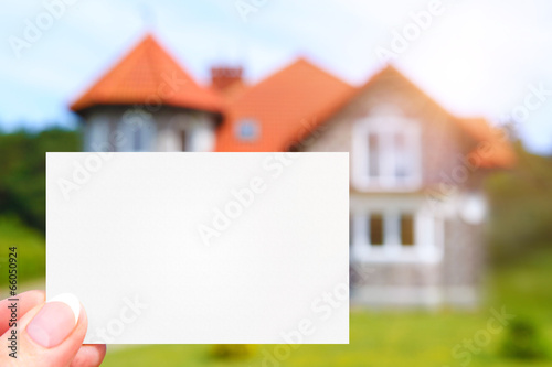 hand holding visit card with house as a background