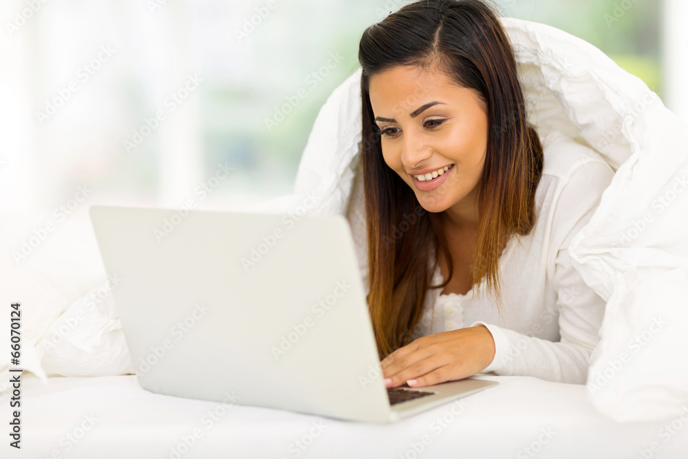 woman using laptop computer while lying on her bed woman using laptop computer while lying on her bed