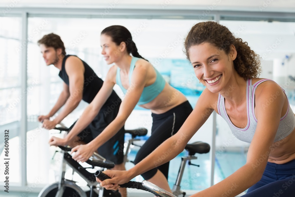 Fit people in a spin class with woman smiling at camera Fit people in a spin class with woman smiling at camera