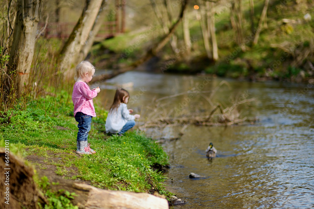 Two adorable sisters feeding ducks by a river Two adorable sisters feeding ducks by a river