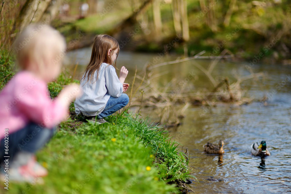 Two adorable sisters feeding ducks by a river Two adorable sisters feeding ducks by a river