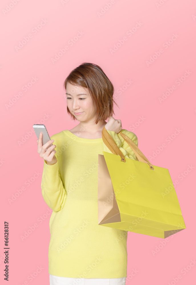 買い物袋を持ちながらスマホを使う女性 買い物袋を持ちながらスマホを使う女性