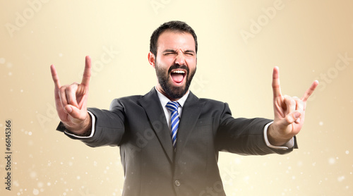 Fotografia Young businessman doing the horn sign over ocher background